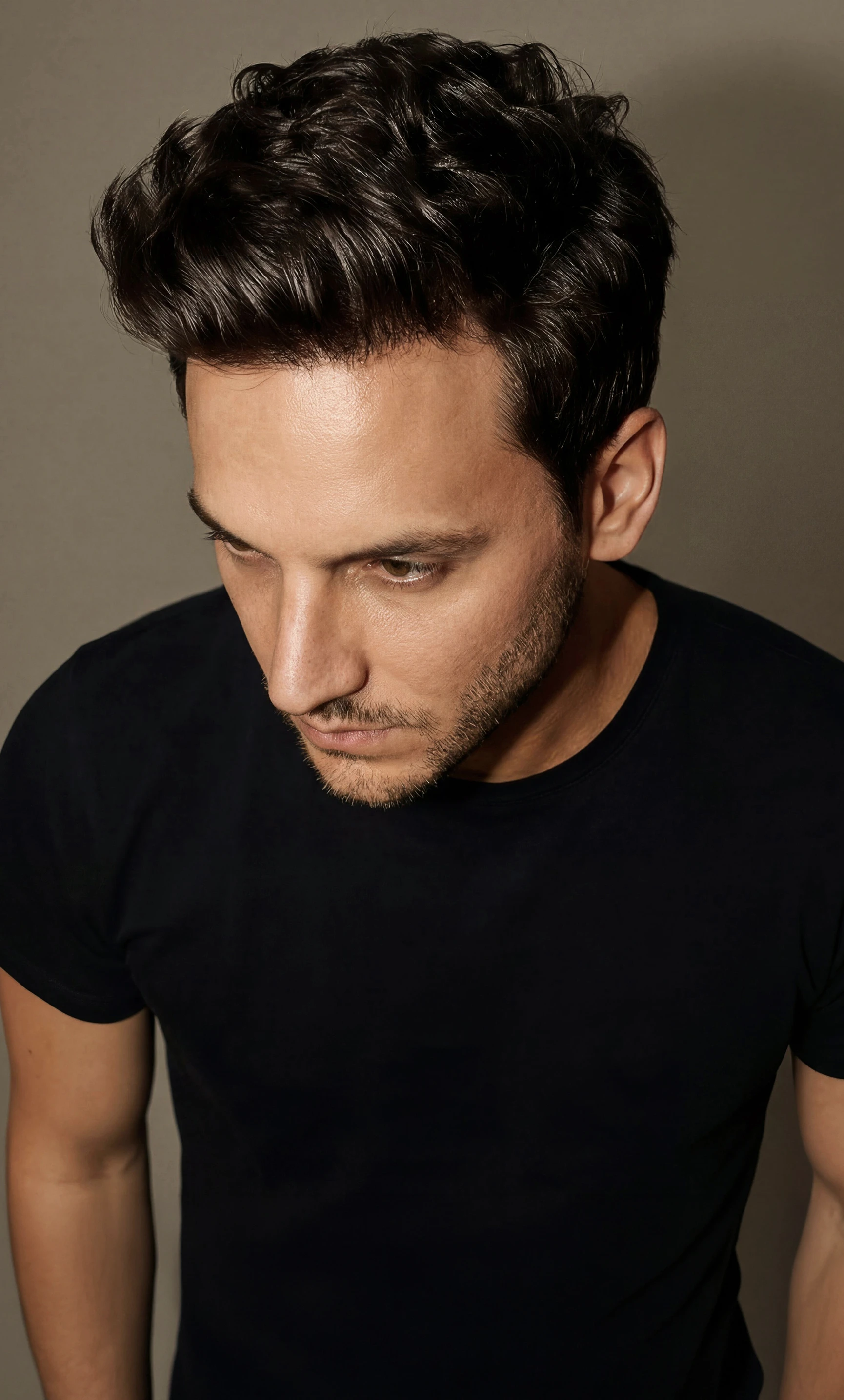 Danny Wave in a black shirt, looking down in a color portrait.